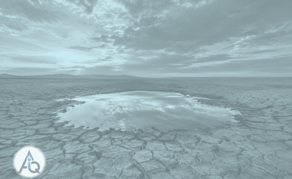 Wijd landschap van gebarsten droge aarde tot aan de horizon onder een dramatische lucht, met in het midden een ondiepe heldere waterpoel die de wolken weerspiegelt