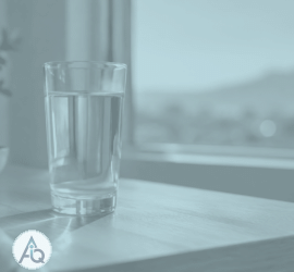 Een hoog glas helder water op een lichte houten tafel bij een raam met zacht blauw ochtendlicht